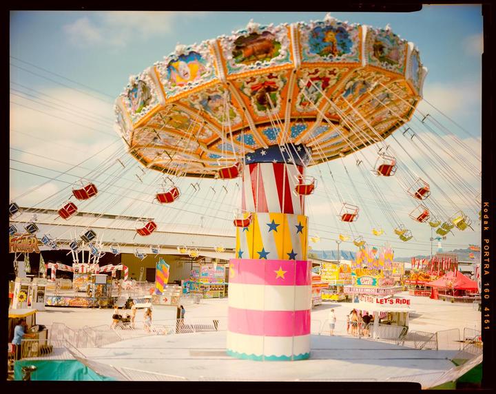 A large swing ride with colorful decorations stands tall at a fairground under a bright sky.