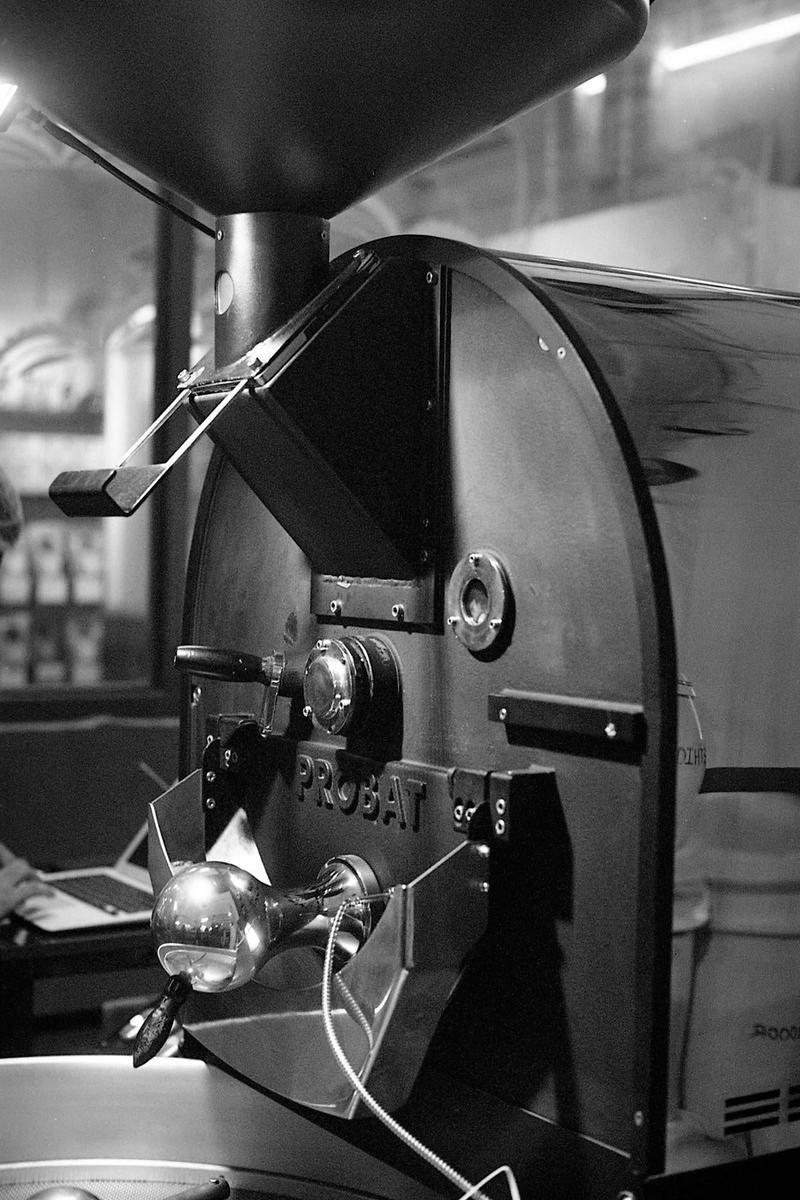 A large coffee roasting machine with a hopper on top is shown in black and white.