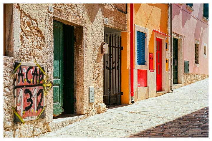 A narrow street is lined with colorful buildings and a graffiti-covered utility box.