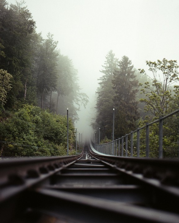 A train track ascends into a foggy forest.