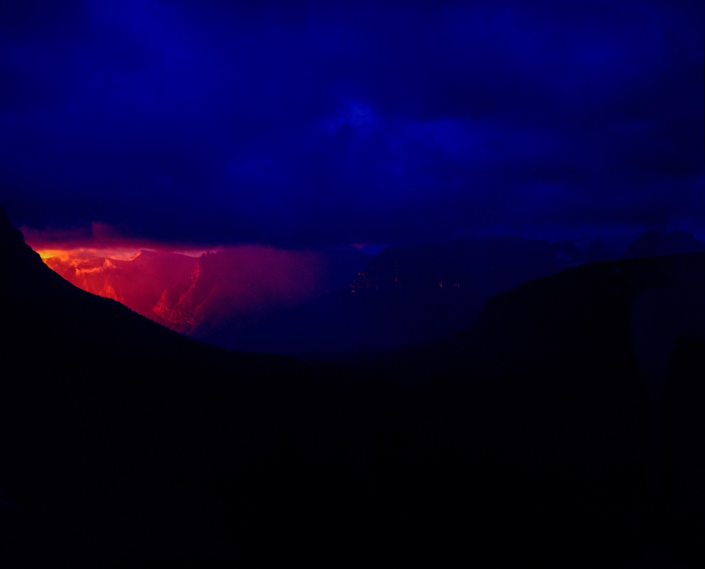 A vibrant sunrise illuminates a mountain range under a dark blue sky.