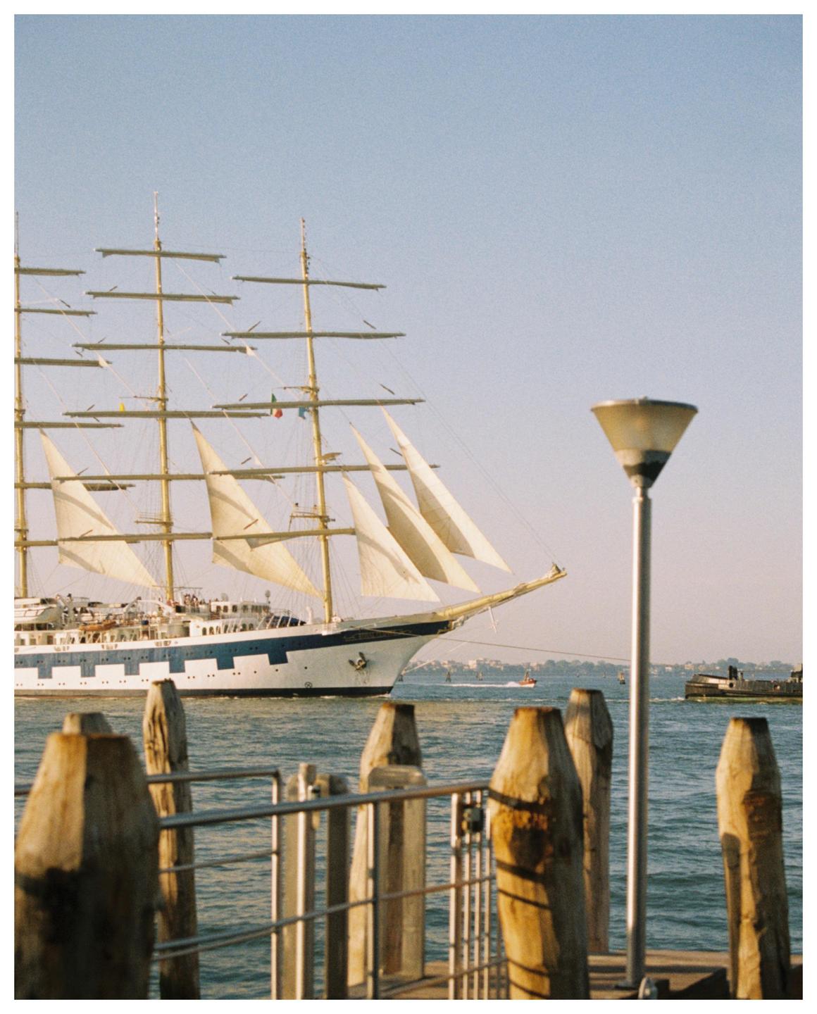 A large sailing ship with multiple masts and sails is visible from a pier with wooden posts and a lamp.