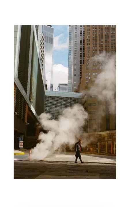 A person walks on a city street with steam rising from a manhole.