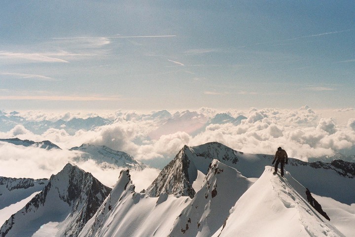A man stands on a snowy mountain peak overlooking a vast expanse of clouds and mountains.