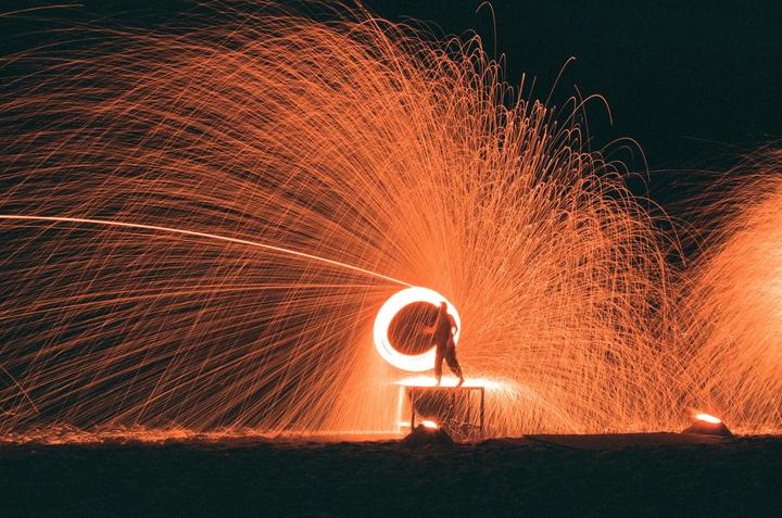 A person stands on a platform surrounded by a shower of orange sparks at night.