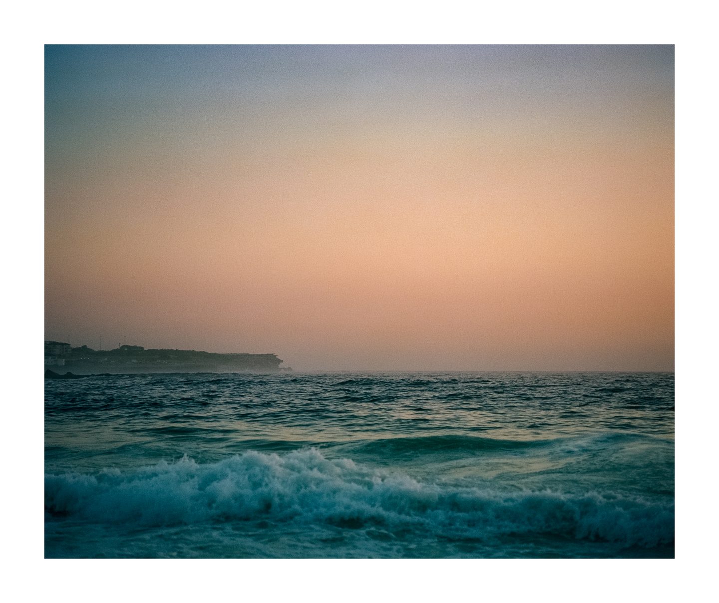 Waves crash on the shore of Coogee Beach under a hazy orange sky.