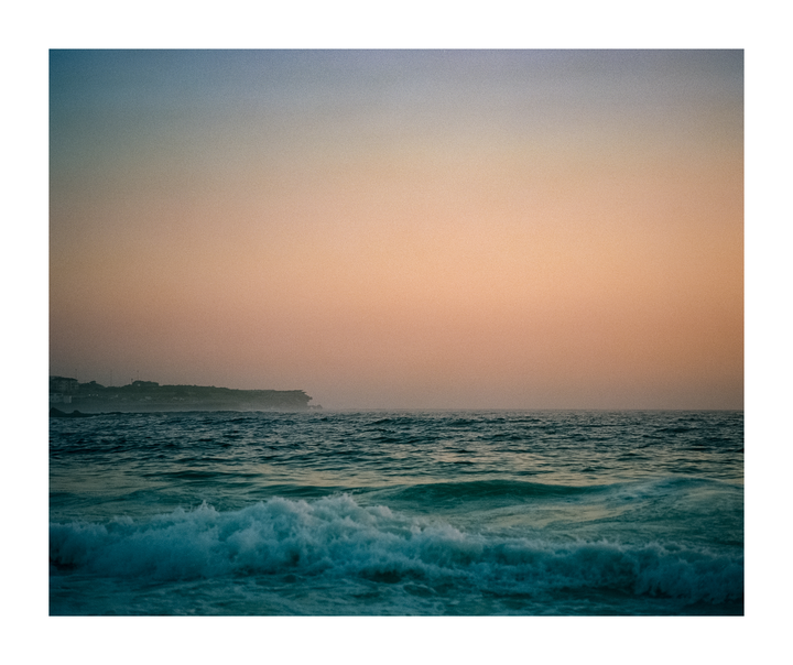 Waves crash on the shore of Coogee Beach under a hazy orange sky.