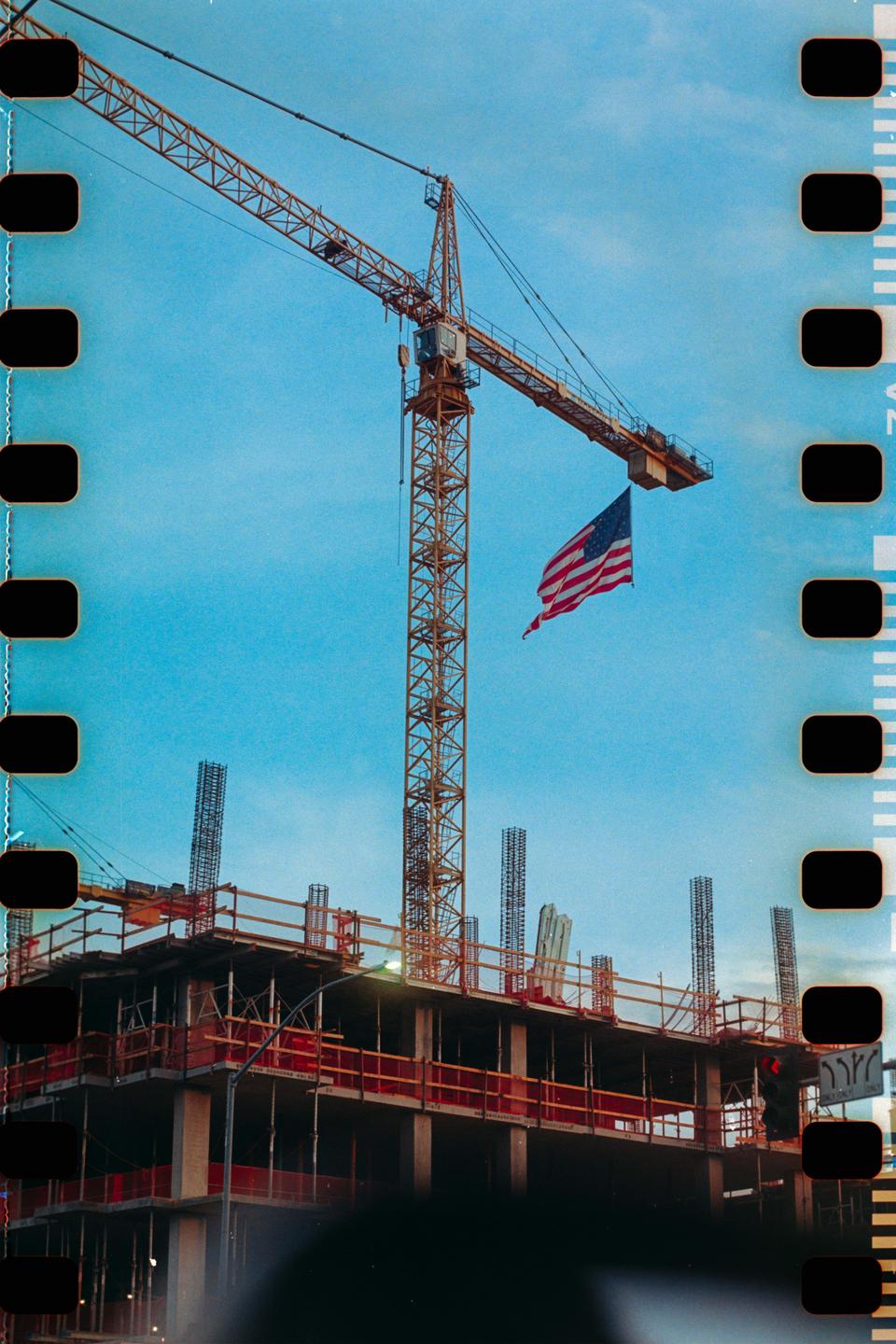 A construction crane with an American flag hanging from it stands over an unfinished building.