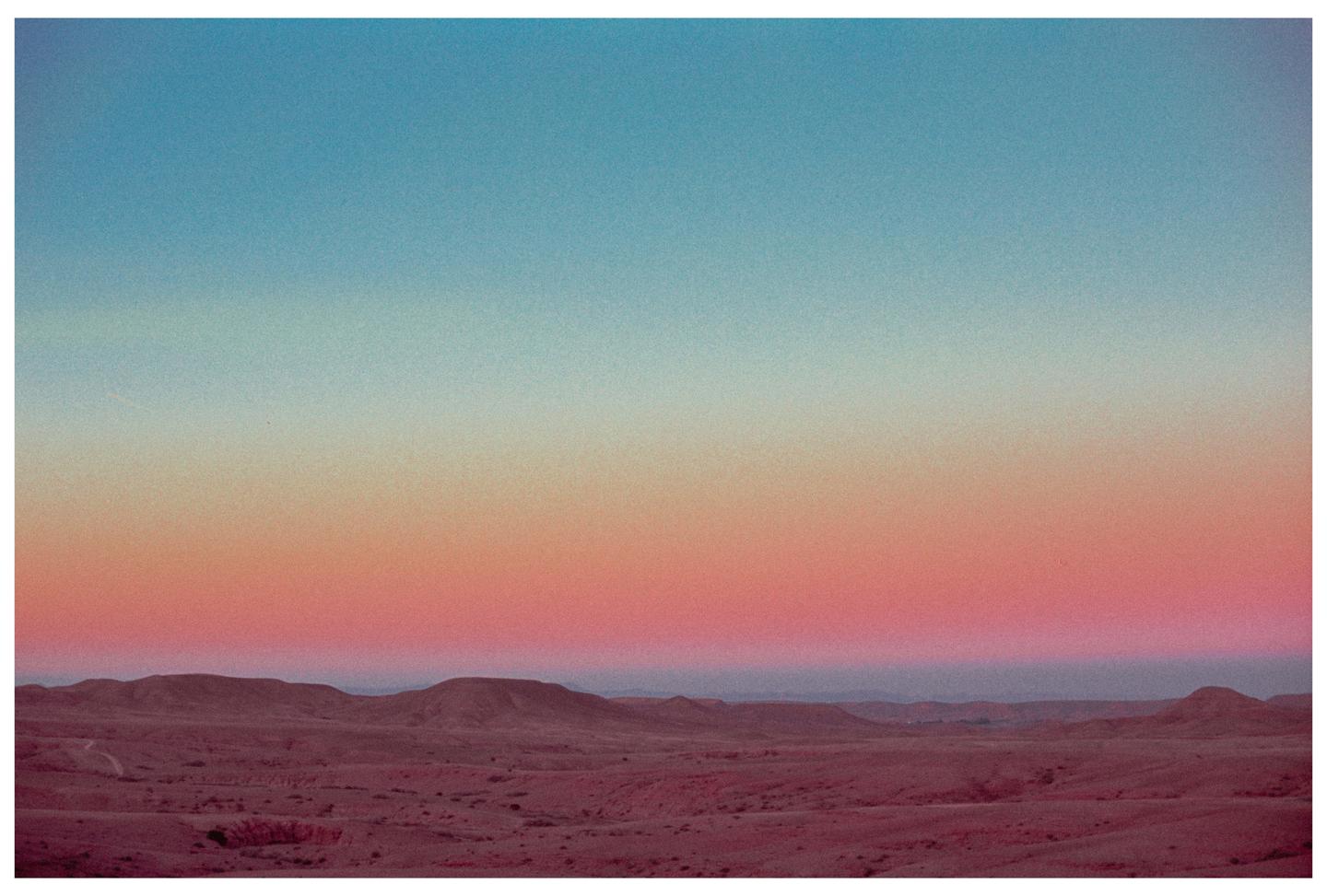 A desert landscape with rolling hills is visible under a sky with a colorful gradient.