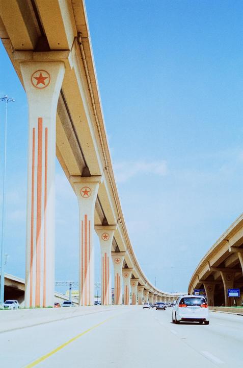 A highway with an elevated road supported by pillars decorated with stars is shown under a clear blue sky.