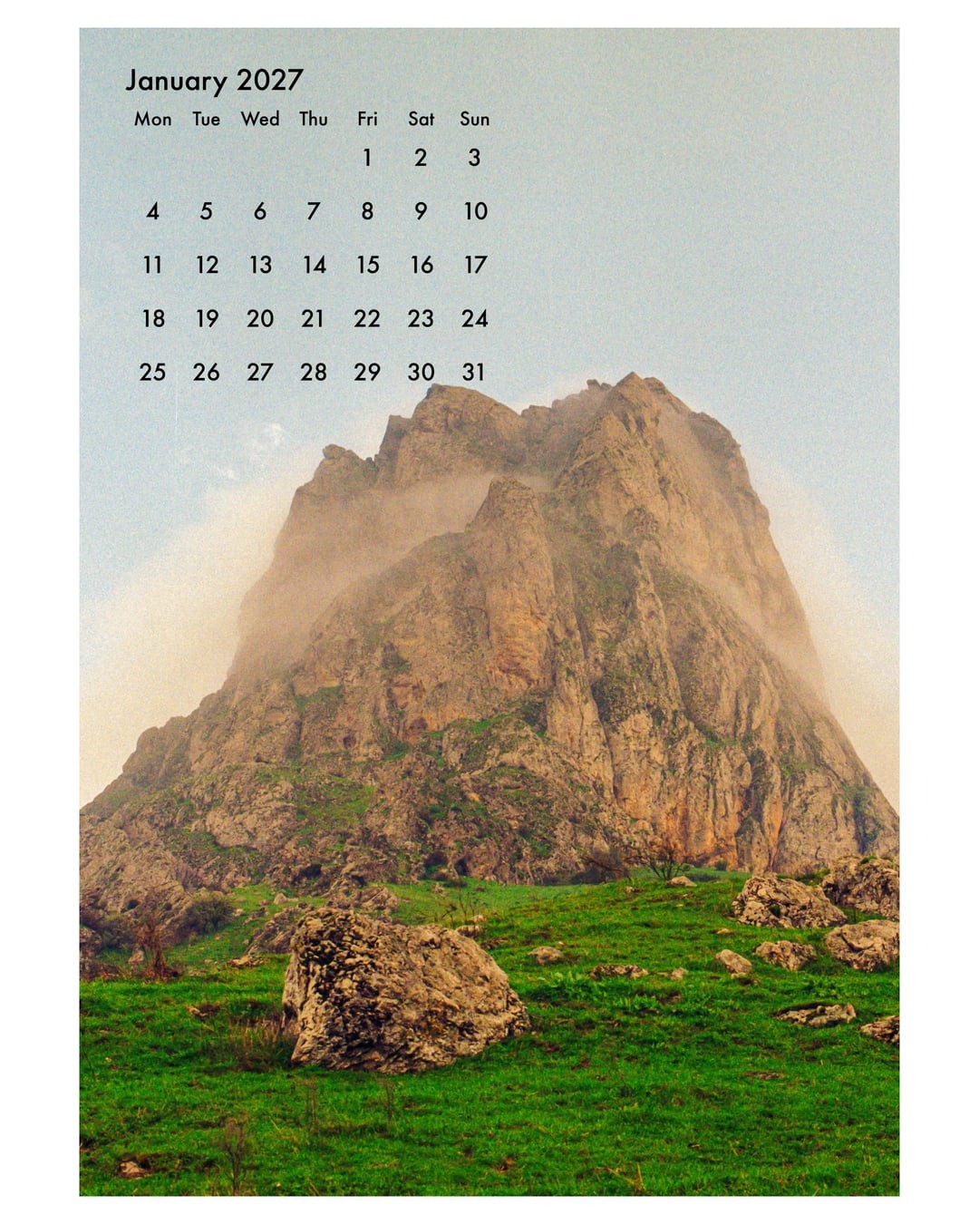 A calendar for January 2027 is superimposed over a mountain landscape with green grass and large rocks.