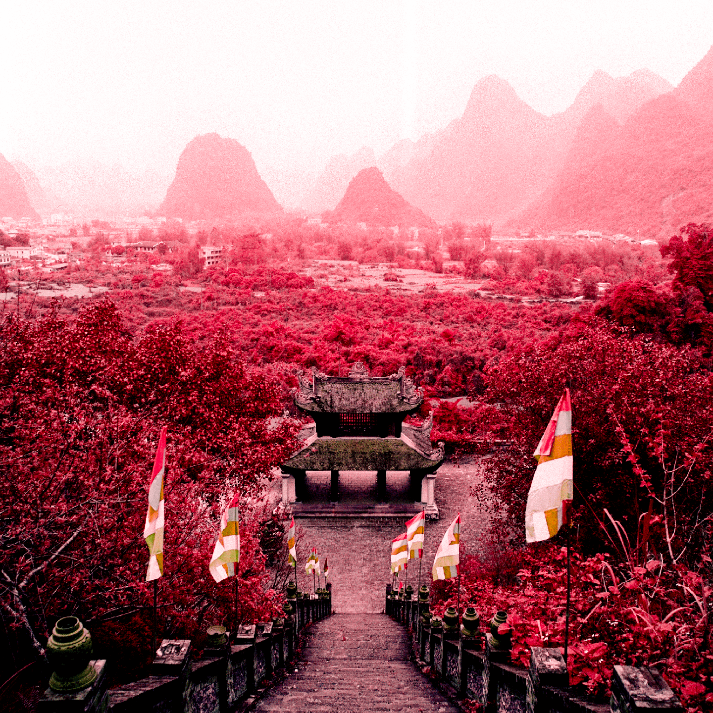 A temple sits at the bottom of a long staircase, surrounded by red foliage and distant mountains.