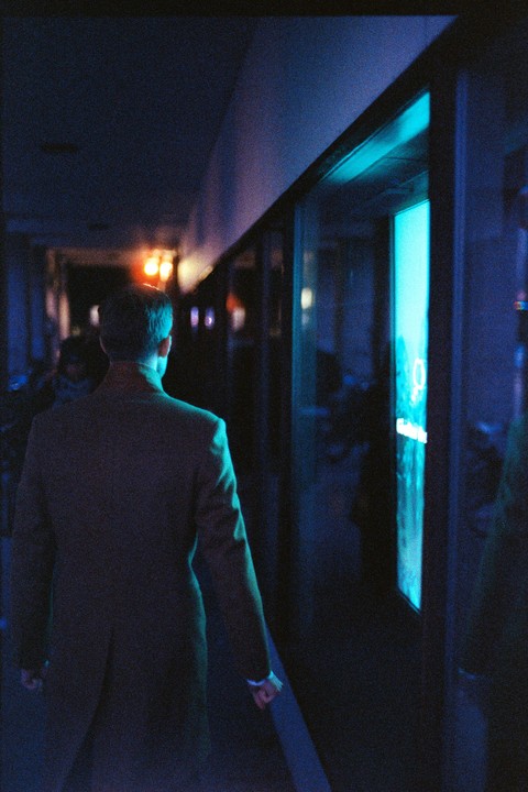 A man in a suit walks down a dark hallway with blue and orange light.