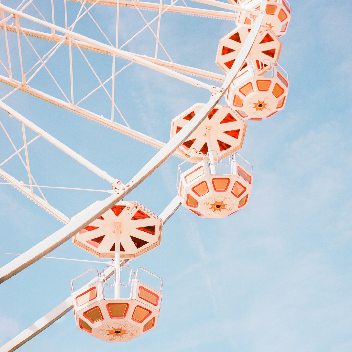 A white ferris wheel with red and orange gondolas is set against a clear blue sky.
