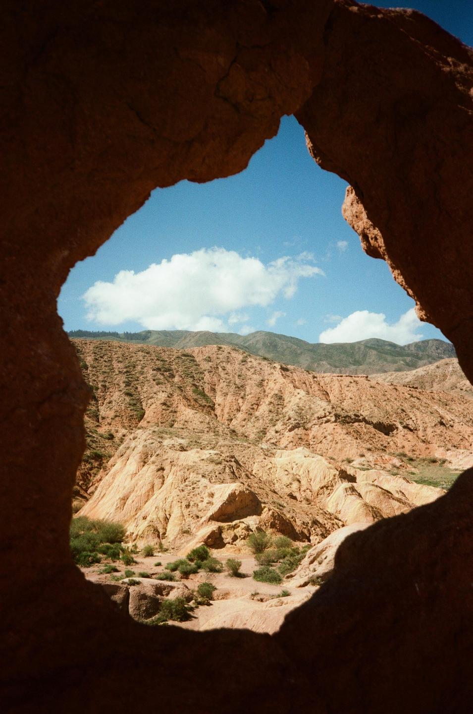 A view of a mountainous landscape with sparse vegetation is framed by a dark rock formation.