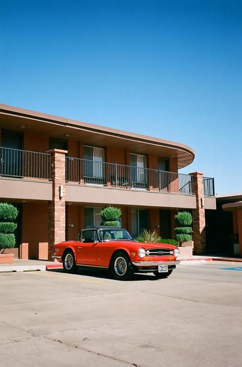 A red convertible car is parked in front of a two-story motel building with balconies.