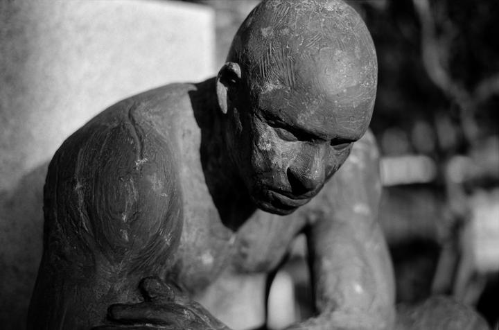 A close-up, black and white shot shows a statue of a man with his head bowed and his hands clasped.