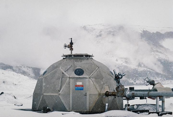 A geodesic dome structure with pipes attached to its side stands in a snowy, mountainous landscape.