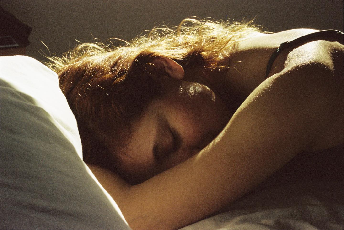 A woman with red hair is sleeping on a pillow, illuminated by warm light.