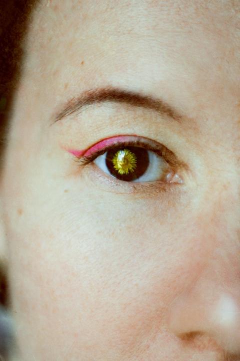 A woman's eye with a dandelion in place of the iris is visible in a close-up shot.