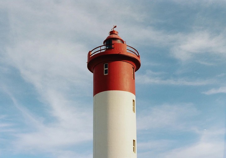 A red and white lighthouse stands tall against a blue sky with wispy clouds.