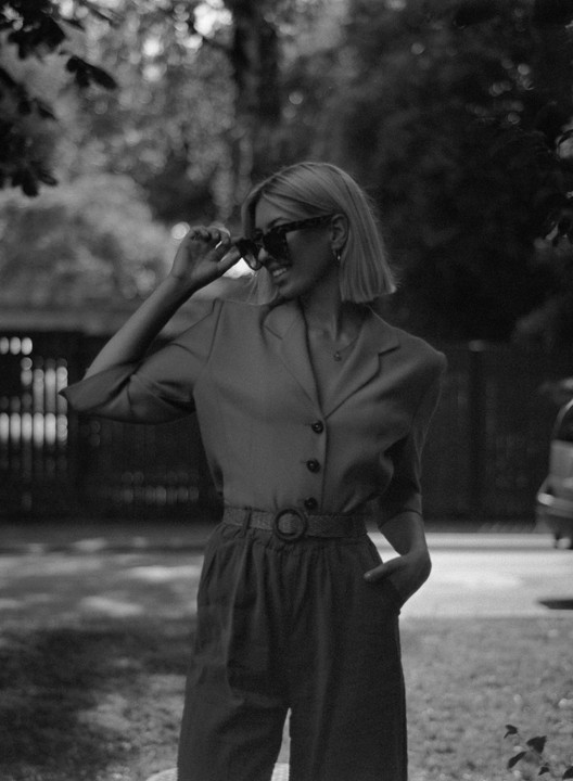 A woman with short hair and sunglasses smiles while standing outdoors.