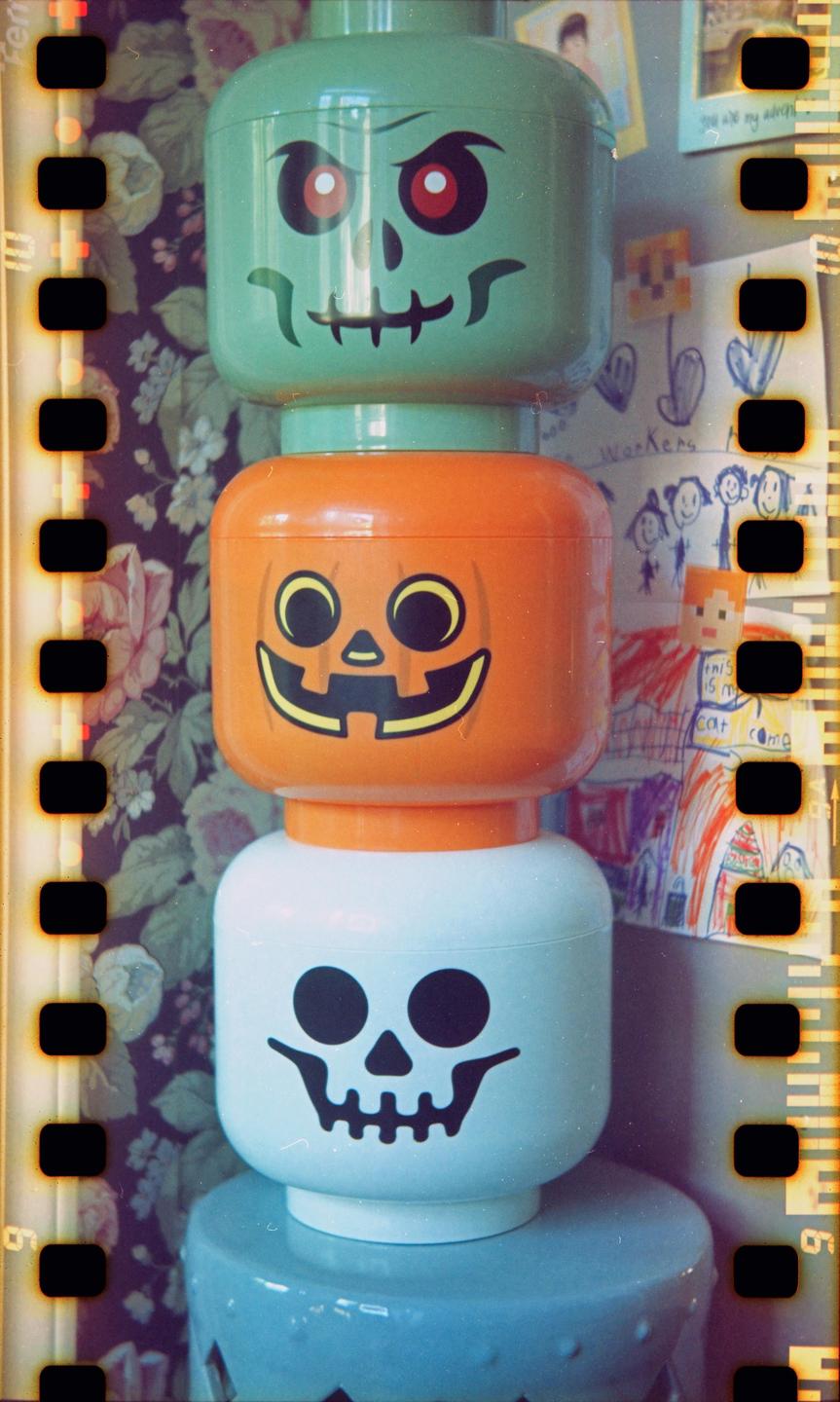 Three stacked Halloween-themed Lego heads are visible with a floral wallpaper background and children's drawings.