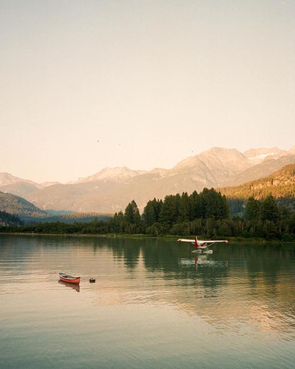 A red canoe and a seaplane are on a lake surrounded by mountains and forest.