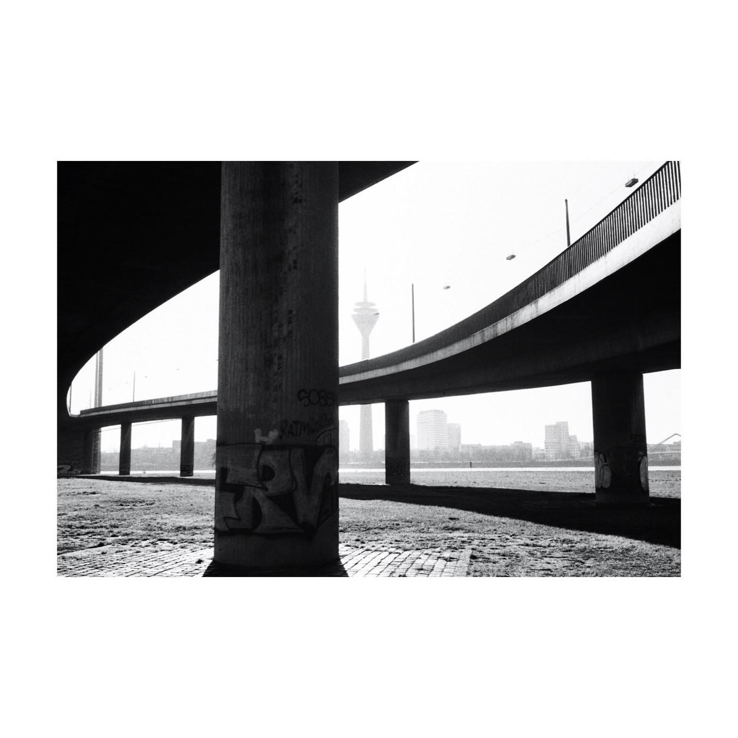 A television tower is visible in the distance through the arches of a concrete bridge.