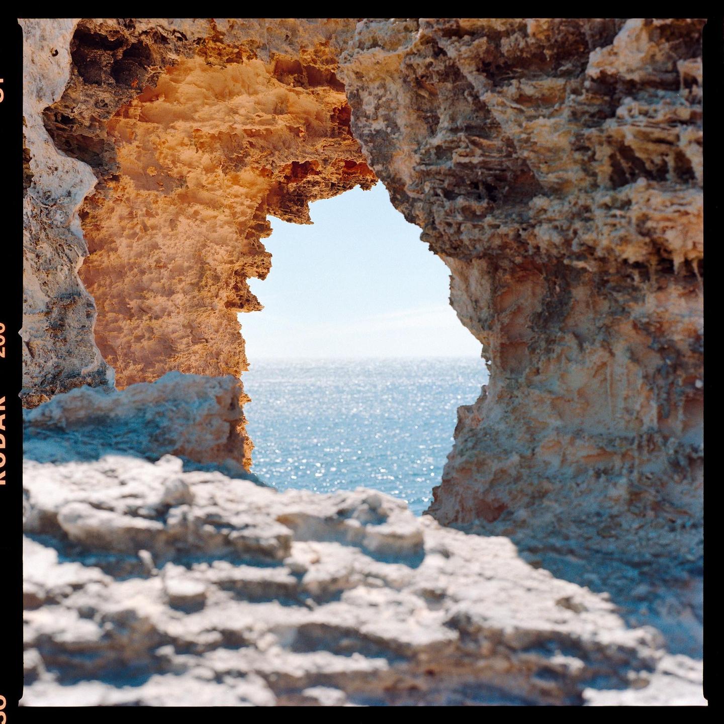 A natural rock arch frames a view of the sparkling ocean under a clear sky.