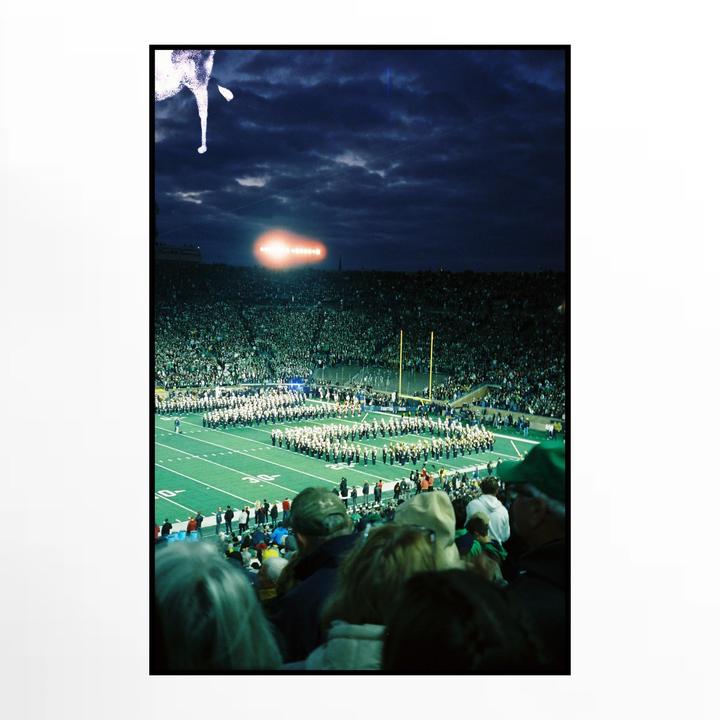 A marching band performs on a football field at night in a stadium filled with spectators.