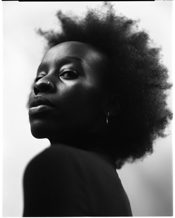 A woman with curly hair and a nose ring looks over her shoulder.