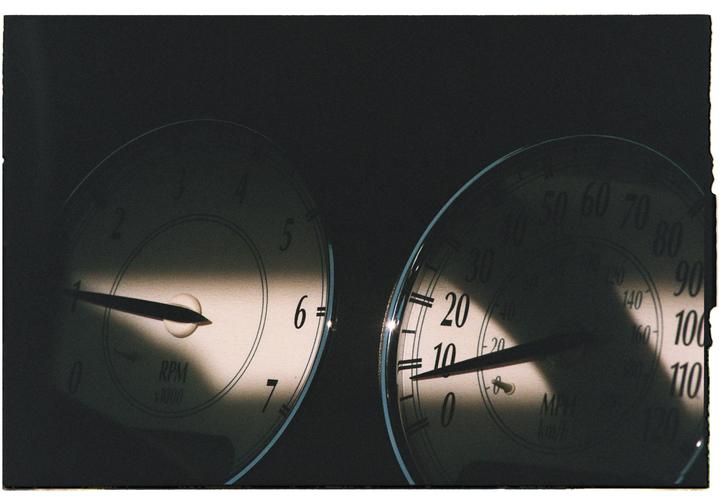 Two vehicle gauges are partially illuminated by a diagonal beam of light.