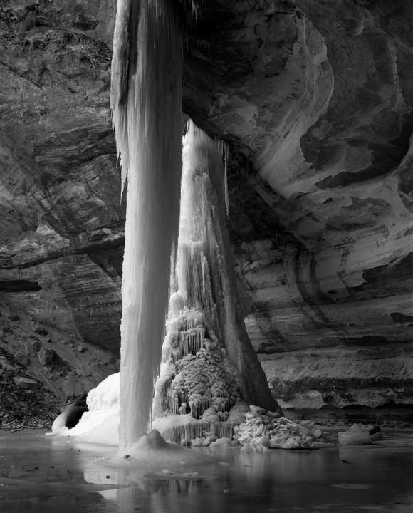 A large icefall descends into a partially frozen body of water within a rocky cavern.