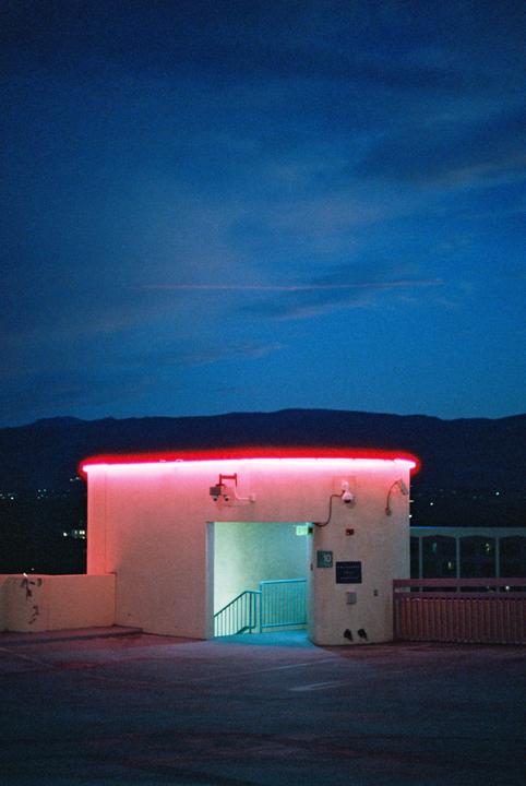 A building with red neon lights on its roof stands against a dark blue sky with mountains in the distance.