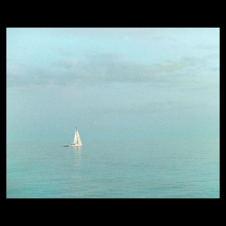 A sailboat floats on a calm body of water under a hazy sky.