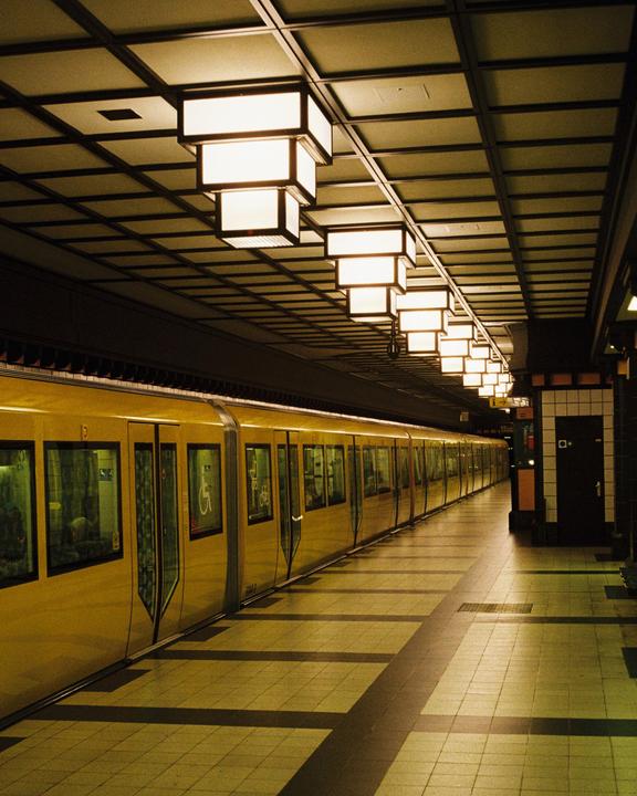 A yellow subway train is stopped at a station platform with bright rectangular lights on the ceiling.