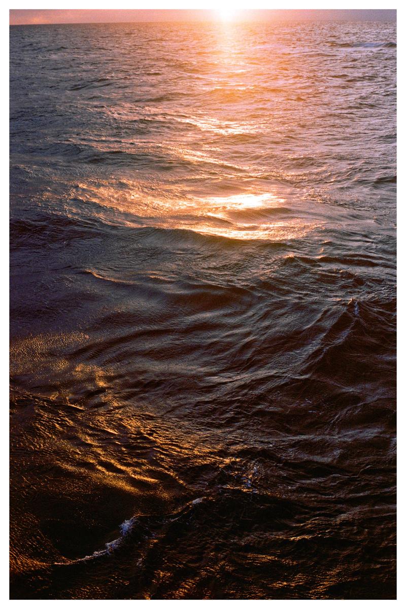 The sun sets over the ocean, casting an orange glow on the water.