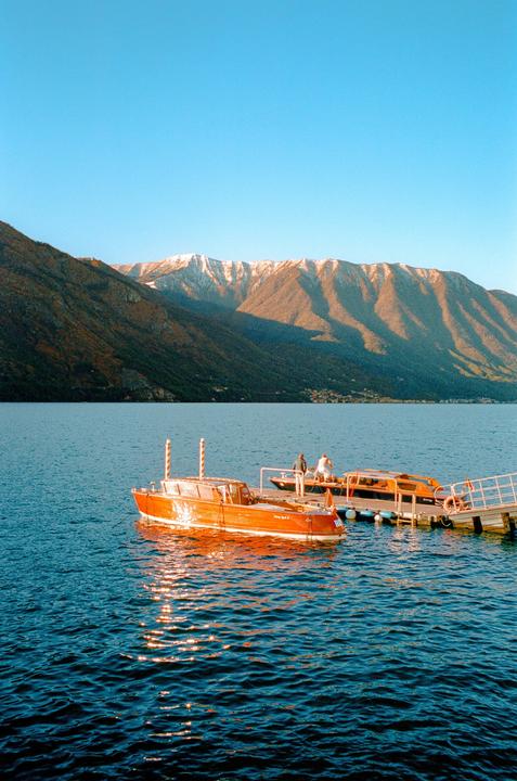 Two boats are docked at a pier on a lake with mountains in the background.