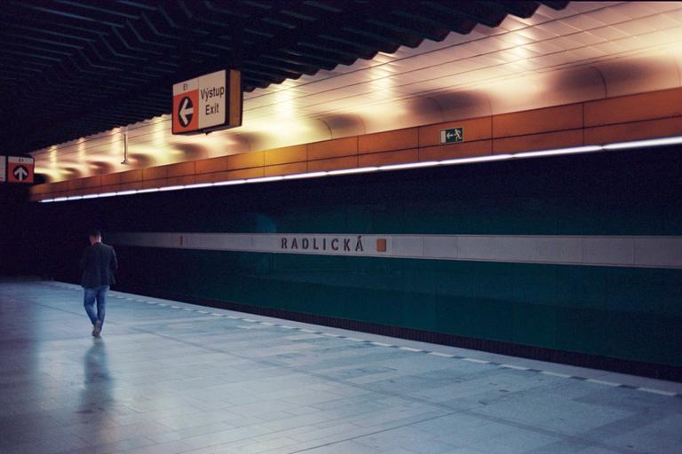 A man walks away from the camera on a subway platform with an exit sign and the station name "Radlická" visible.