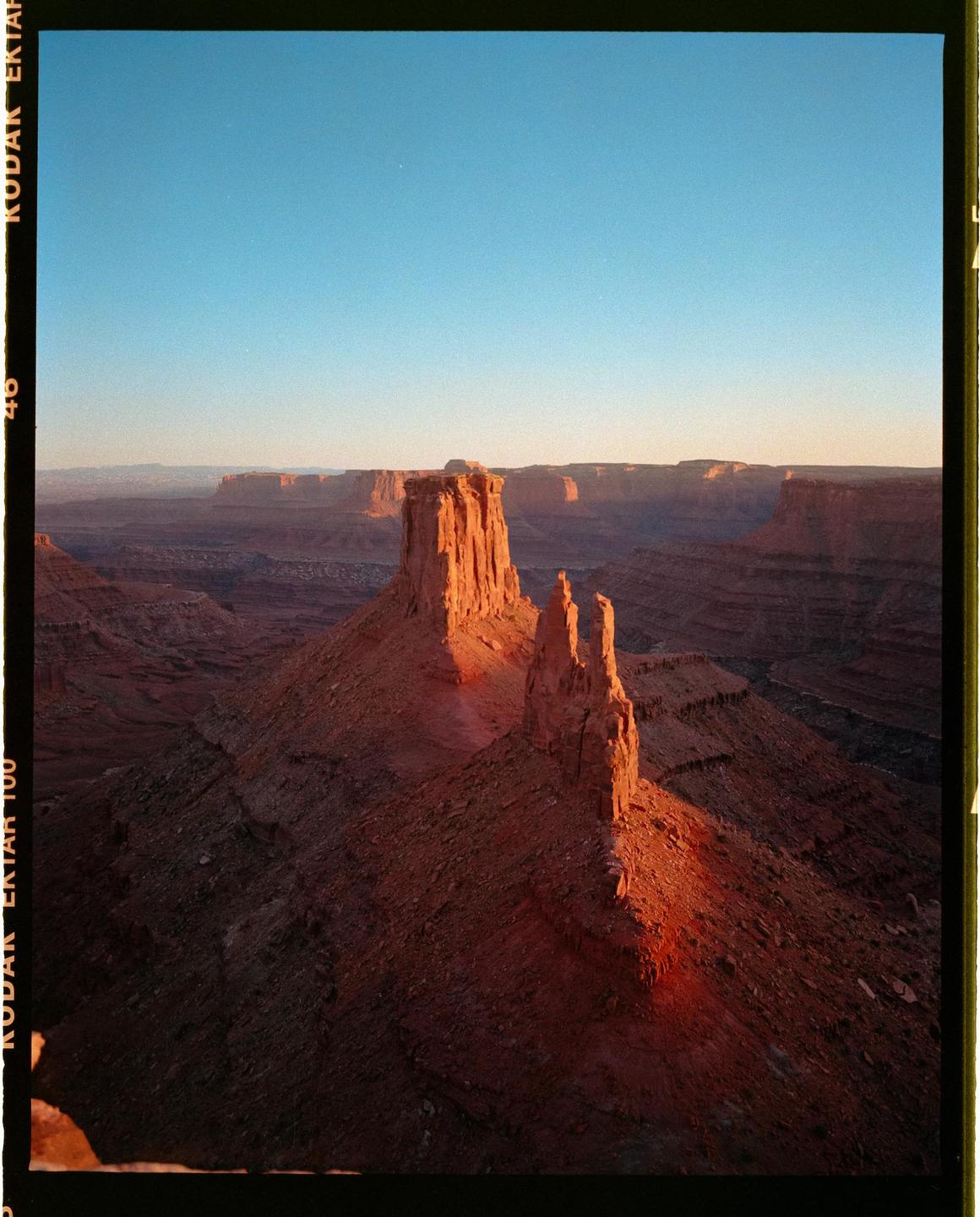 A vast canyon landscape is illuminated by the golden hour light, highlighting several rock formations.