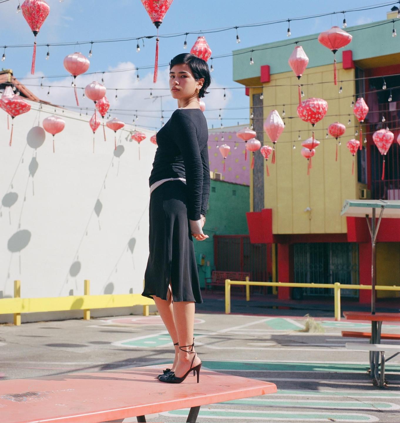 A woman stands on a red picnic table in an outdoor area decorated with red lanterns.