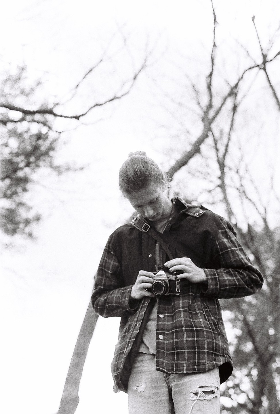 A man with a bun in his hair looks down at a camera he is holding in his hands.