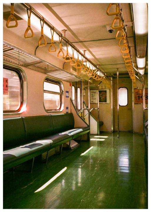 Sunlight streams into an empty subway car with green seats and floor.