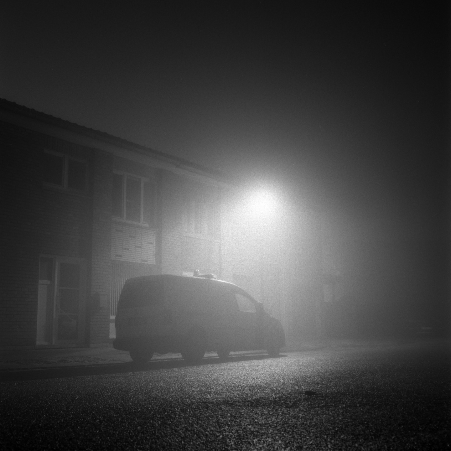 A van is parked on a street in front of a building on a foggy night.