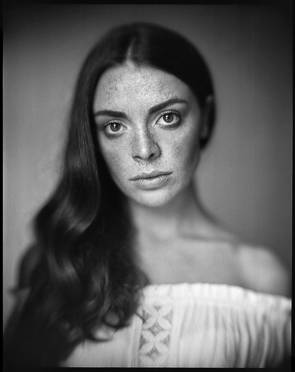 A woman with long hair and freckles looks directly at the viewer.