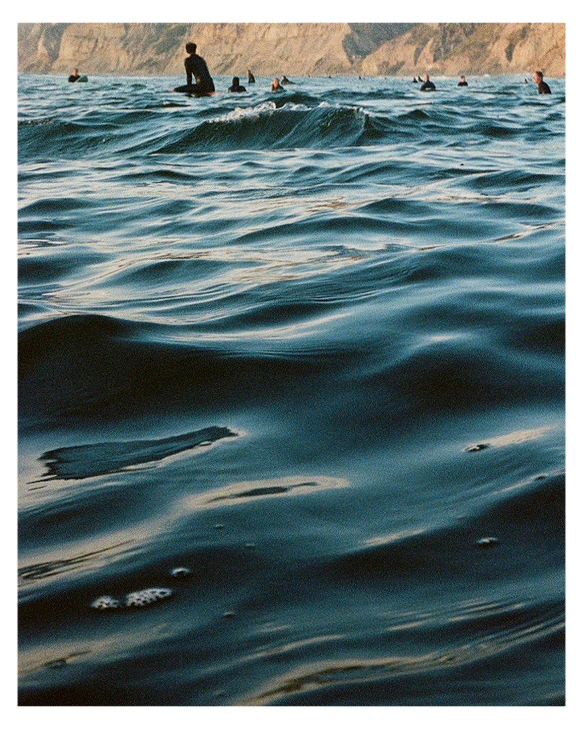 A group of surfers are in the ocean with a cliff in the background.