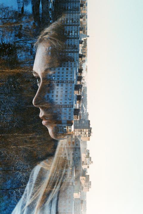 A woman's profile is double exposed with a cityscape and a forest.