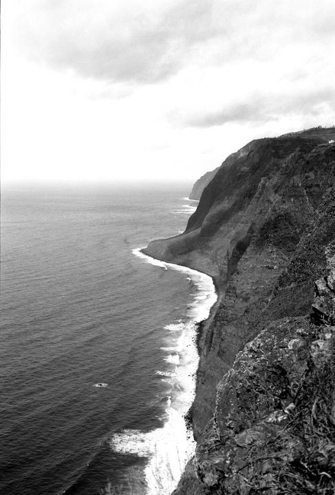 A black and white landscape shows a long coastline with cliffs meeting the ocean under a cloudy sky.