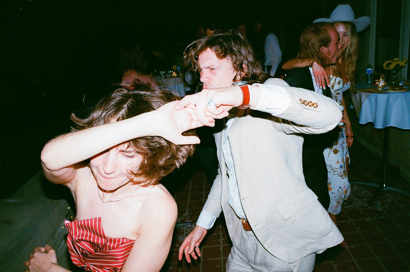 A woman in a red striped top covers her face with her arm while a man in a suit jacket dances next to her.